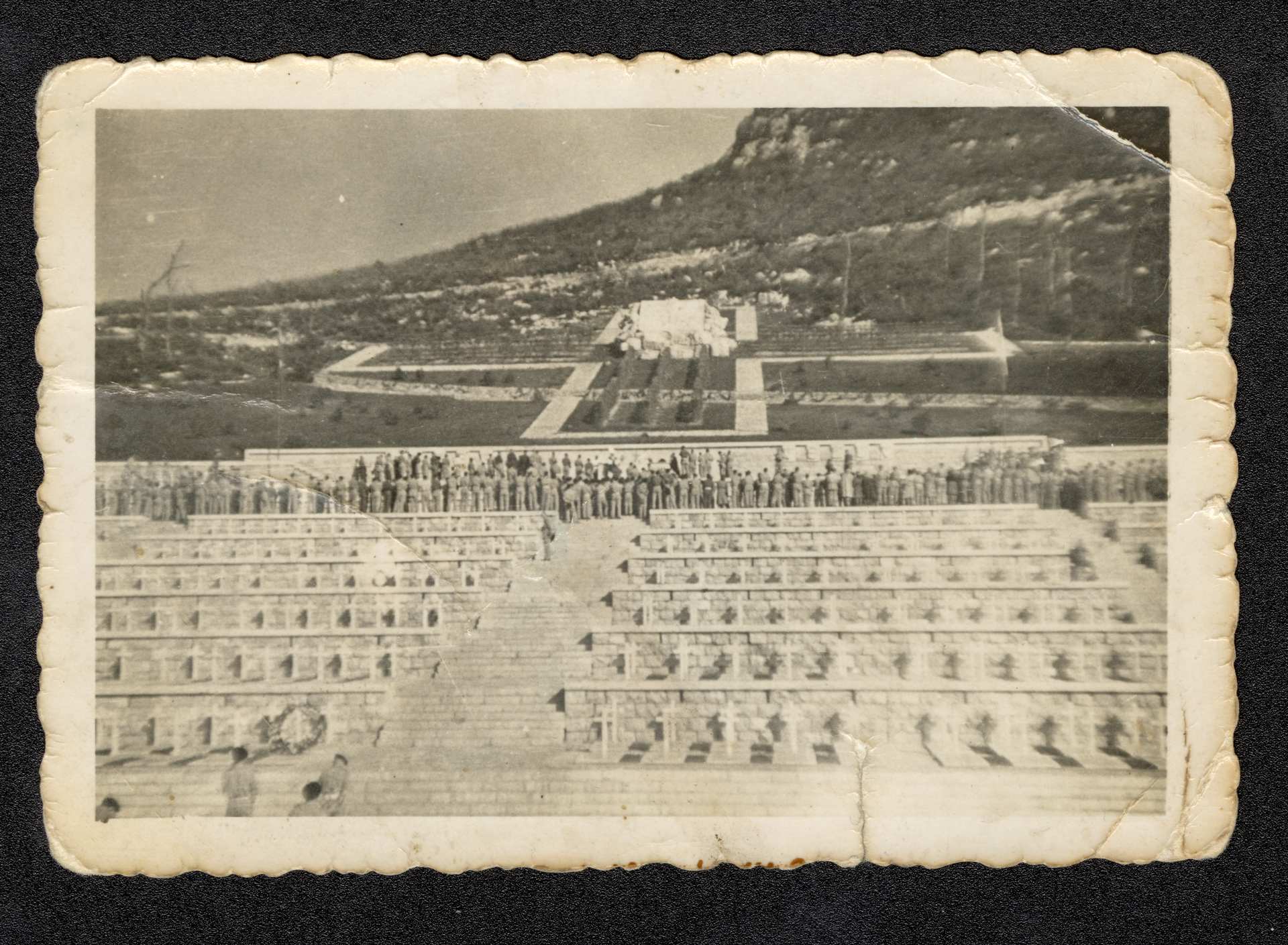 Na zdjęciu widać cmentarz na tle gór i stojącą tyłem grupę żołnierzy