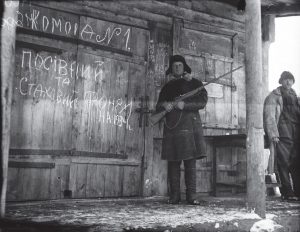Zdjęcie przedstawia komunistycznego aktywistę pilnującego jakiegoś pomieszczenia. W ręce trzyma karabin.