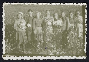 Na zdjęciu widać osiem dziewcząt stojących na łące. Trzymają w rękach kłęby bawełny