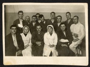 Na zdjęciu widać kilkanaście stojących i siedzącychosób, wśród nich dwie pielęgniarki i mężczyzna w białym kitlu