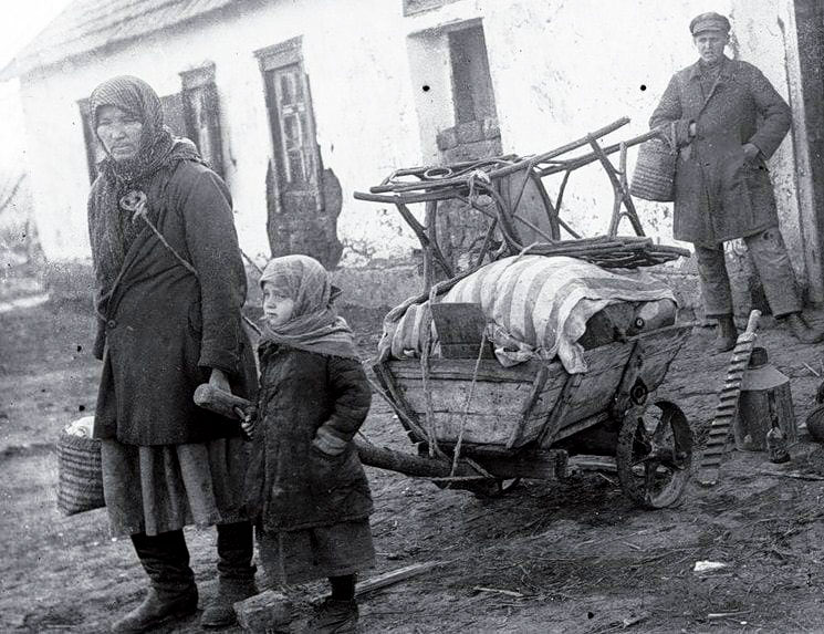 Na zdjęciu widac kobietę z dzieckiem ciągnącą wózek z dobytkiem