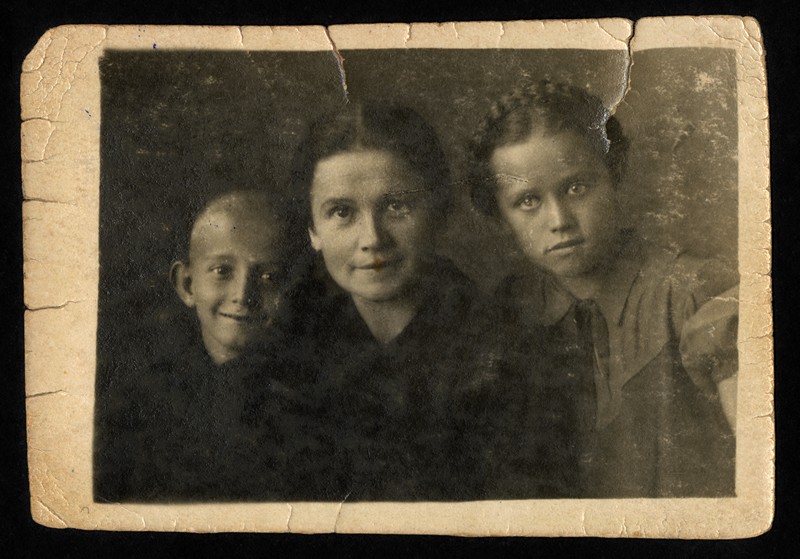 Na zdjęciu są od lewej strony: chłopiec z jasnymi włosami, w środku kobieta, z prawej strony dziewczynka z warkoczem owiniętym wokół głowy