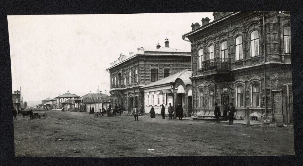 Na czarno-białym zdjęciu widać murowane domy stojące przy ulicy i przechodniów