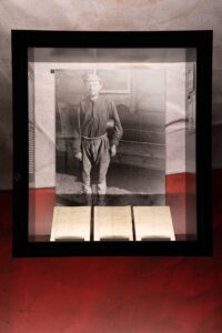 Na zdjęciu widac gablote szklaną ze zdjęciem stojącego mężczyzny w zniszczonym ubraniu