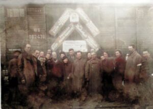 Na zdjęciu widać grupę kobiet i mężczyzn stojących obok wagonu kolejowego ozdobionego napisami