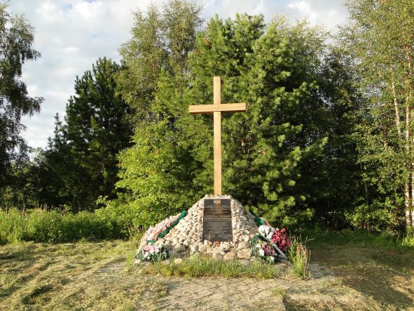 Na zdjęciu widać krzyż i tablice pamiątkową na tle zieleni.