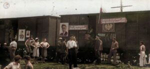 Na zdjęciu widać kobiety i mężczyzn stojących przy wagonach kolejowych ozdobionych napisami i zdjęciami