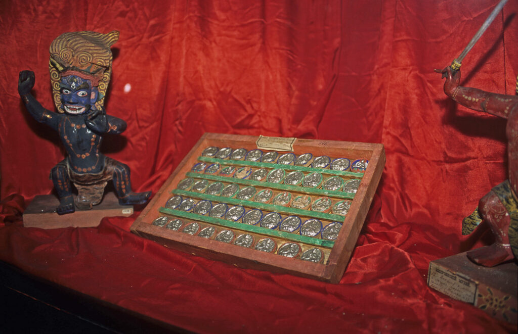 Na zdjęciu widać kolekcję monet w drewnianym pudełku na tle czerwonej materii.
