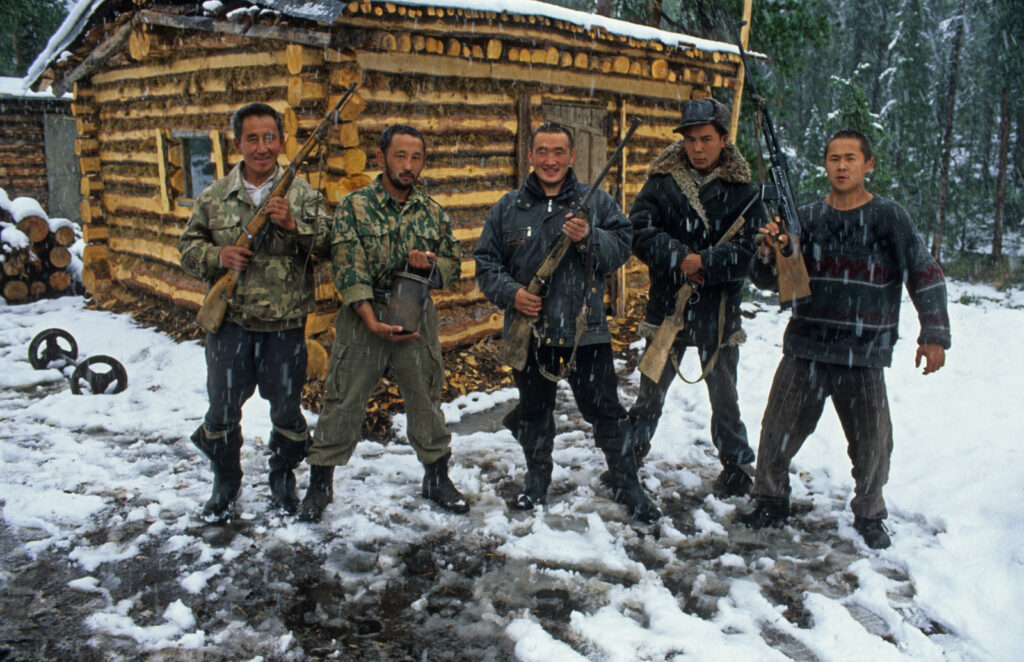 Na zdjęciu widać pięciu mężczyzn z bronią stojących na tle drewnianego budynku
