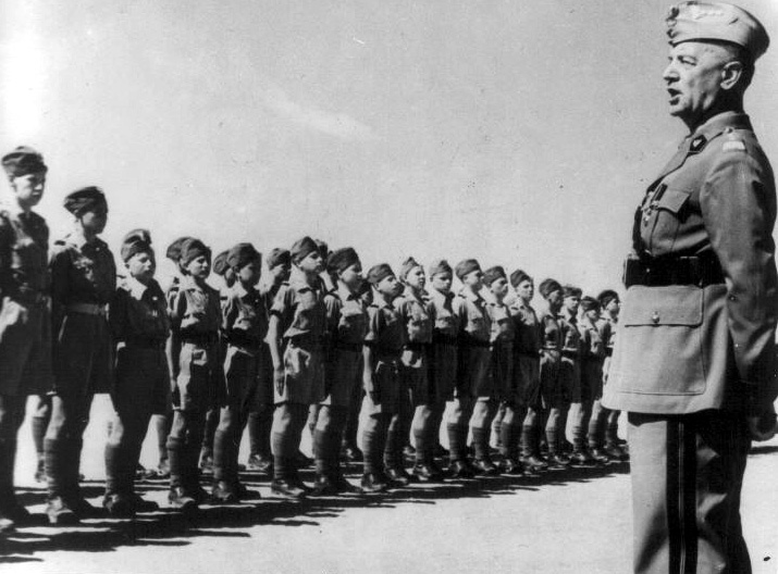 A military man in front of boys in uniforms