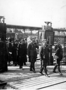 A group of military personnel surrounded by civilians,  carrying an urn