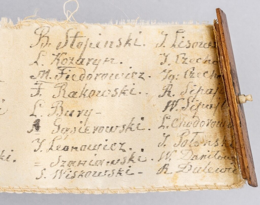 Taśma z materiału z wypisanymi odręcznie nazwiskami w języku polskim