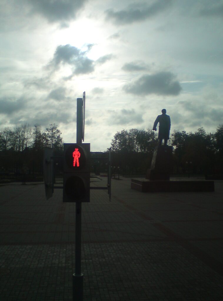 Fotografia przedstawiająca pomnik Lenina i świetlny sygnalizator uliczny pokazujący czerwone światło.